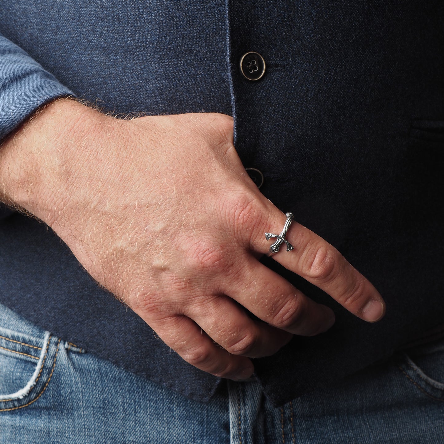a man in a blue vest and jeans with a King Arthur's excalibur sword ring on his index finger