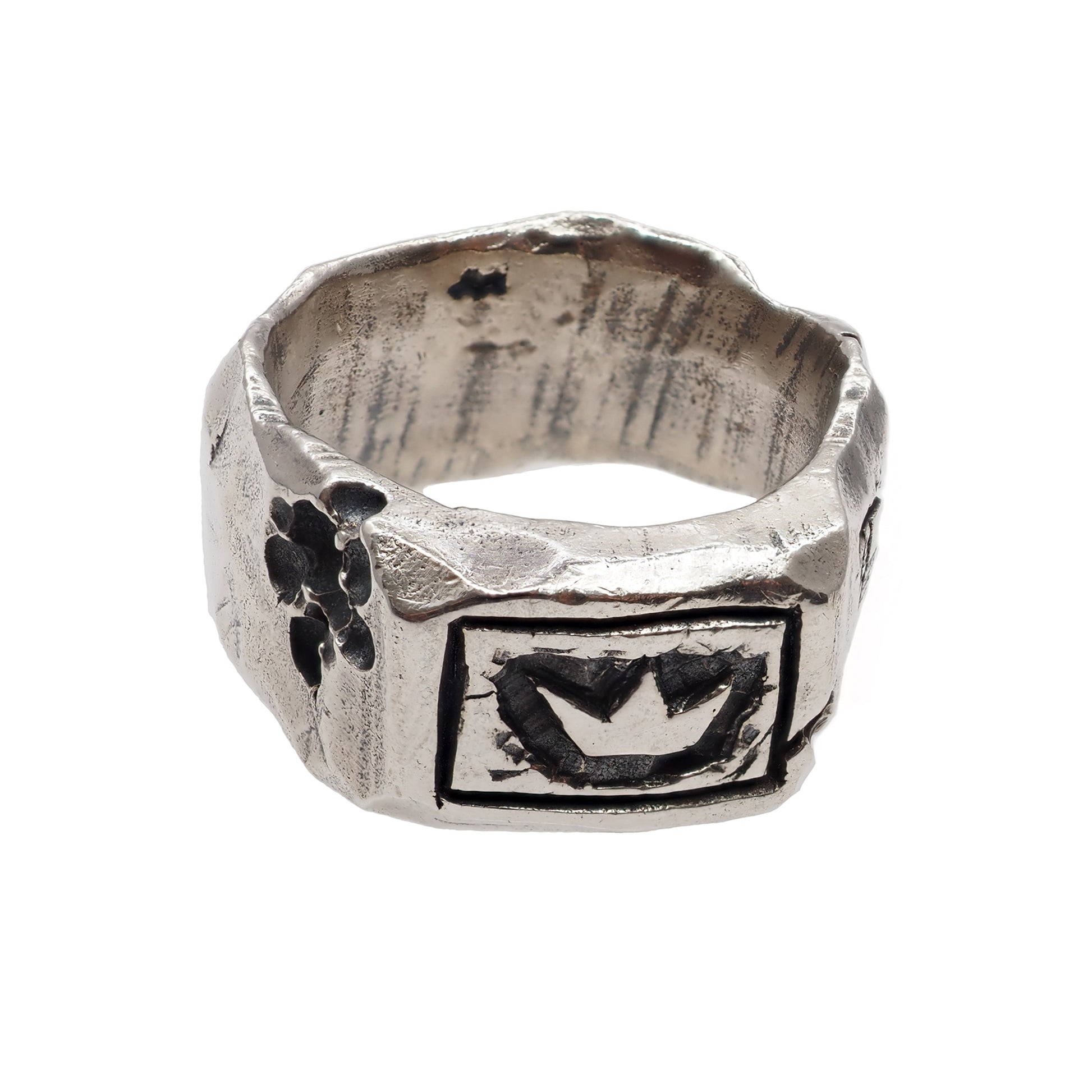 Silver ring of King Arthur with a crown in the foreground and a decorative carved lava flow structure on the left on a white background