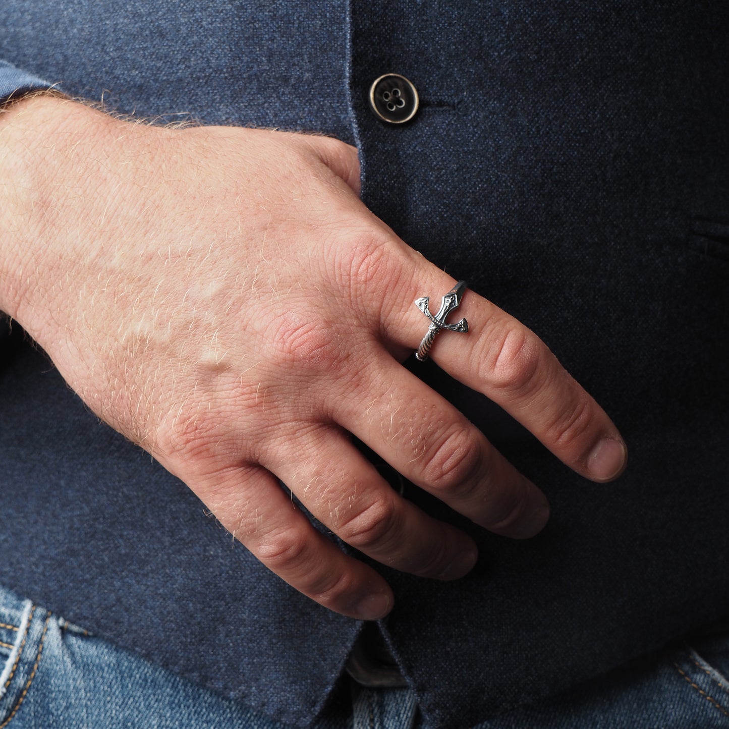 a man in a blue vest with a King Arthur's excalibur sword ring on his index finger