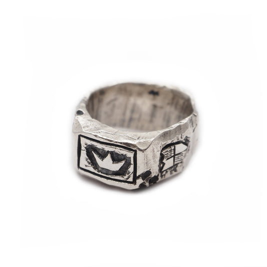 Silver ring of King Arthur with a crown in the foreground and a knight's shield on the right on a white background